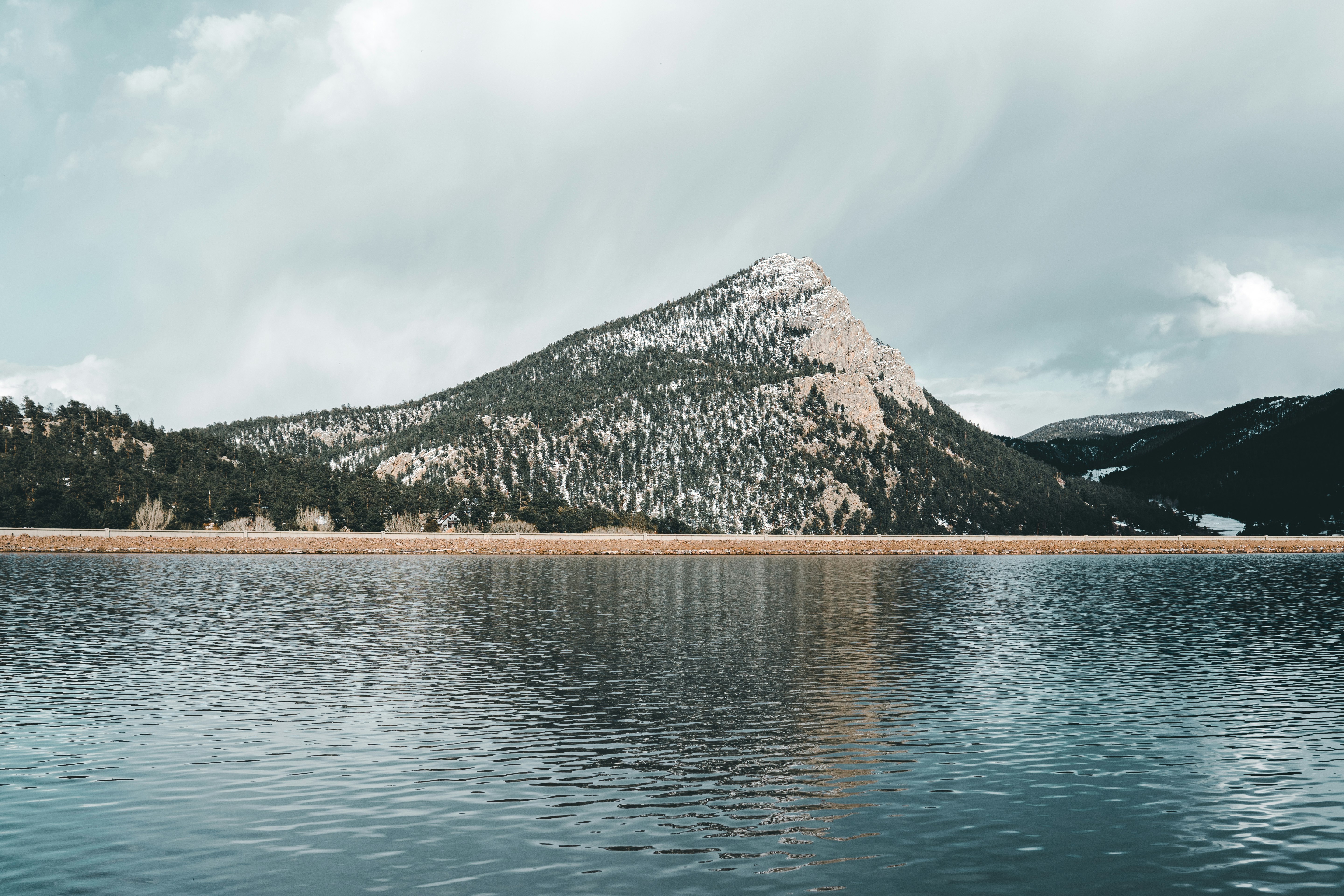 green and brown mountain beside body of water under white clouds during daytime